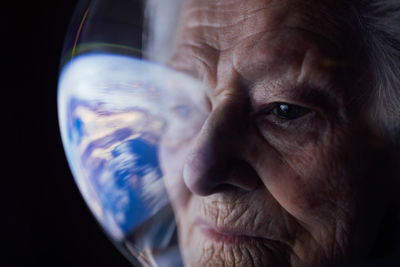 Closeup of concentrated elderly female in spacesuit in space suit looking at earth and thinking about future of globe