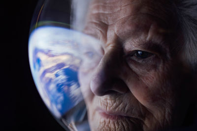 Closeup of concentrated elderly female in spacesuit in space suit looking at earth and thinking about future of globe
