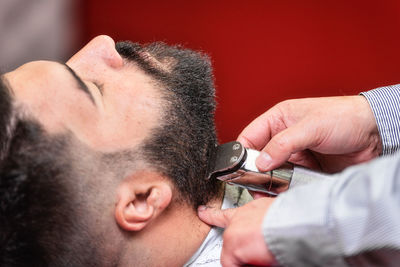 Cropped hands of barber shaving male customer beard in salon