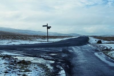 Snow covered road by field against sky