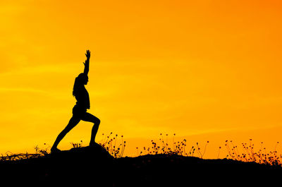 Silhouette woman exercising on mountain against orange sky