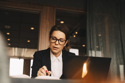 Low angle view of serious female financial advisor reading book at table in law office