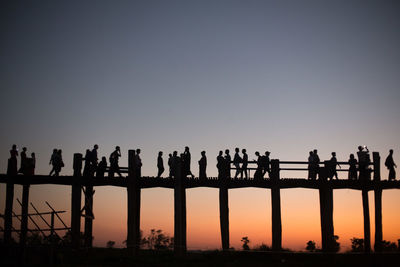 Silhouette people on bridge against clear sky during sunset