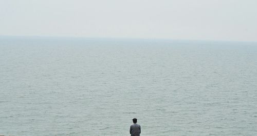 Rear view of man looking at sea against clear sky