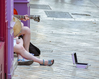 Low section of people playing musical equipment sitting on footpath