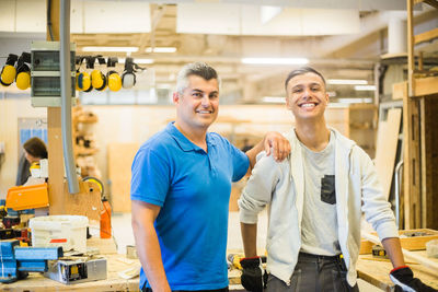 Portrait of smiling male instructor standing with hand on teenage trainee's shoulder at illuminated workshop