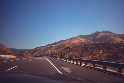 Road by mountains against clear blue sky seen through car windshield