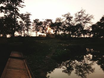 Silhouette trees by lake against sky during sunset