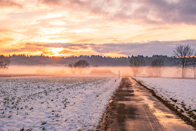 Winter landscape with road, white fields cover by snow and sunset sky.