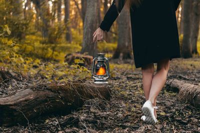 Low section of woman with illuminated lantern walking in forest