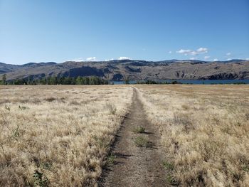 Dirt road amidst field against sky