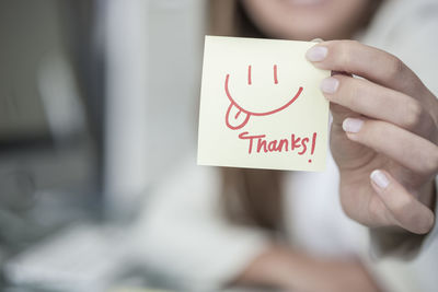 Close-up of woman holding a sticky note with a smiley face