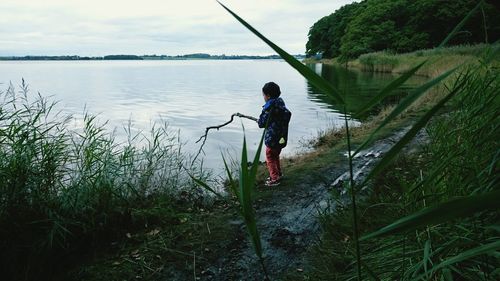 Full length of boy playing with stick at lakeshore