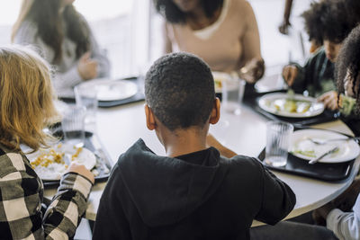 Rear view of boy sitting with friends at table in cafeteria