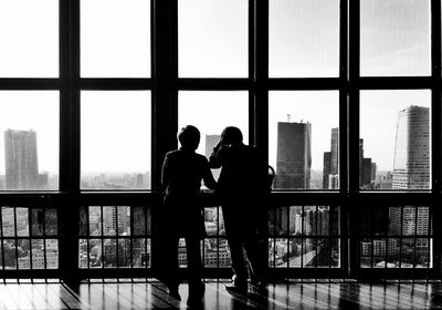 View of friends looking at urban skylines from window of glass building