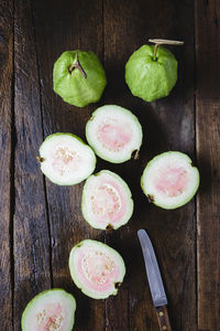 Directly above shot of sliced guavas with table knife on wooden table