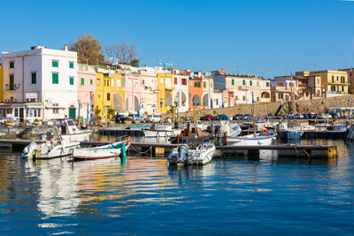 Sailboats moored on canal by buildings against clear blue sky