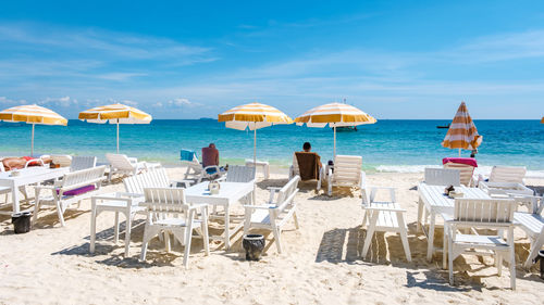 Lounge chairs and tables at beach against sky