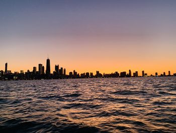 Sea and buildings against clear sky during sunset