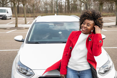 A cheerful african american woman stands next to the white car and laughing