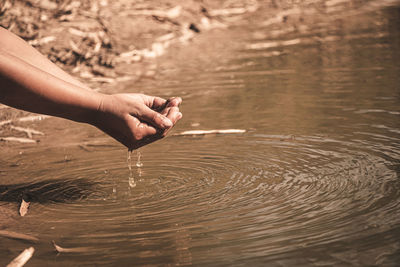Cropped image of hands holding water by lake