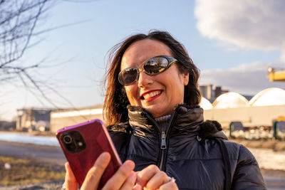 Middle aged woman wearing winter clothes using smartphone in front of a factory - people having fun