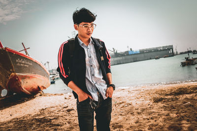 Young man standing on shore against sky