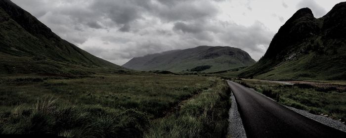 Country road leading towards mountains against sky