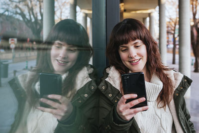 Portrait of happy young woman using mobile phone in winter