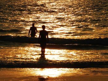 Silhouette people standing in sea against sky during sunset