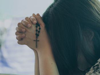 Close-up of woman holding rosary beads and praying