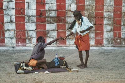 Man giving money to beggar on street against wall