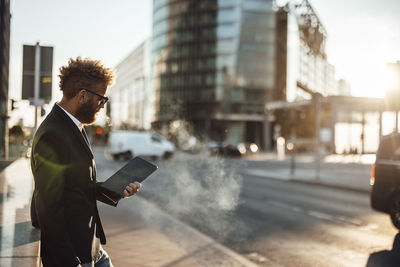 Mature businessman using digital tablet on footpath during sunny day