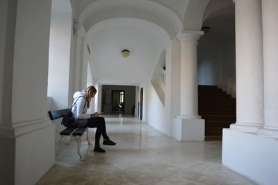 Side view of woman sitting on bench at corridor