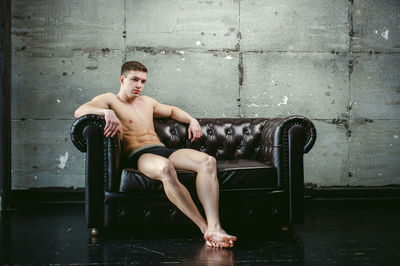 Shirtless muscular man sitting on armchair by wall