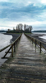 Empty wooden pier amidst trees against sky