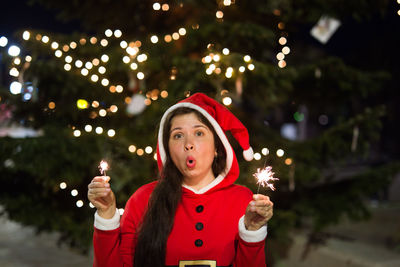 Portrait of teenage girl holding illuminated christmas tree at night