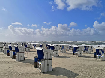 Hooded chairs on beach against sky