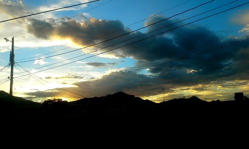 Low angle view of electricity pylon against cloudy sky