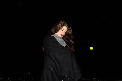 Young woman covered with shawl standing at night