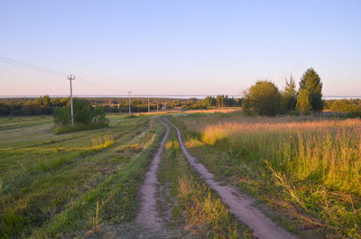 Road amidst field against clear sky during sunset