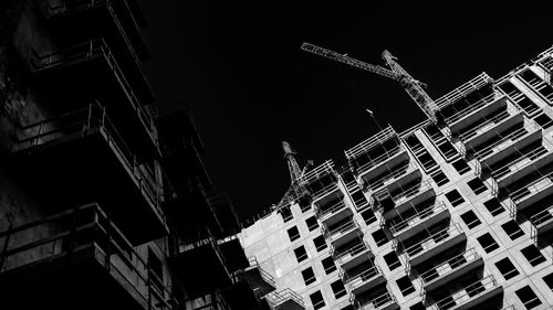 Low angle view of crane by buildings against sky at night