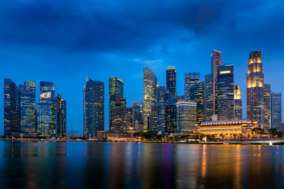 Illuminated modern buildings by bay against sky