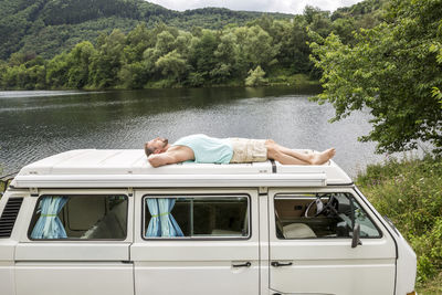 Man lying on roof of a van at lakeside