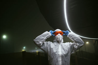 Astronaut holding protective sunglasses against illuminated dark background