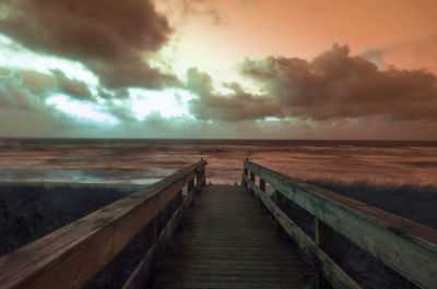 Boardwalk leading towards sea against sky