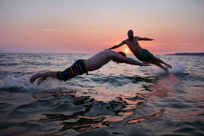Full length of male friends diving in sea during sunset