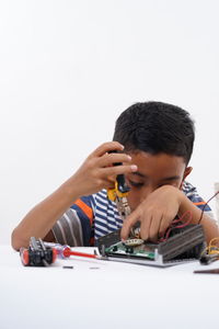 Cute boy repairing electrical equipment on table against white background