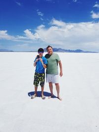 Portrait of father and son standing on white sand against sky