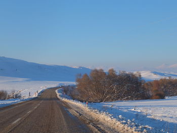 Road amidst snowcapped landscape against sky during winter
